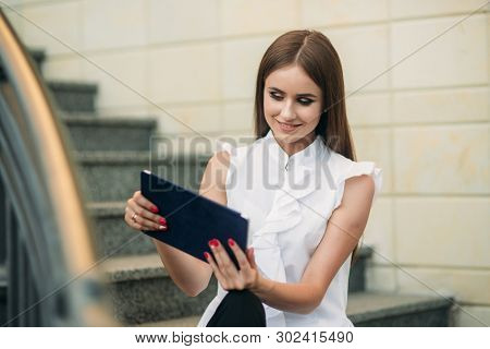 Young And Attractive Female Sittind On The Stairs And Use Tablet. Woman Play Online Games On Tablet