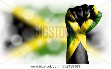 Flag Of Jamaica Painted On Male Fist, Strength, Power, Concept Of Conflict. On A Blurred Background 