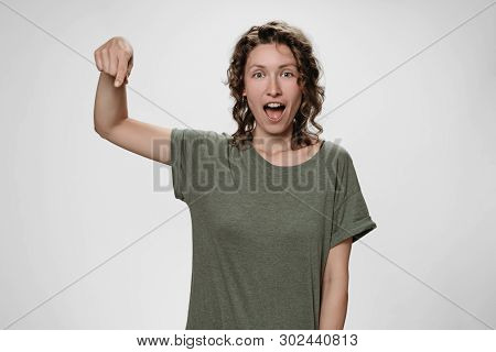 Portrait Of Amazed Woman With Opens Eyes And Mouth Widely Stupefied Expression, Points Down With Ind