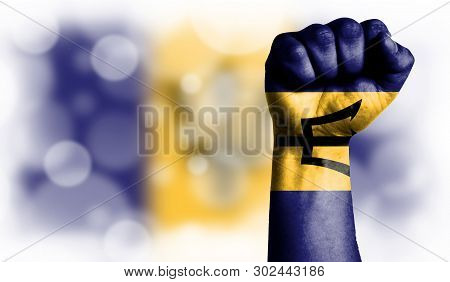 Flag Of Barbados Painted On Male Fist, Strength, Power, Concept Of Conflict. On A Blurred Background