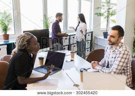 Group Of Young Business People Working, Communicating While Sitting At The Office Desk Together With