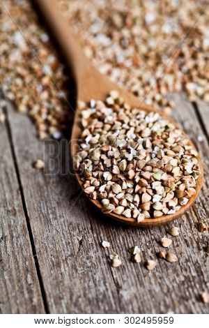 Organic green dry buckwheat seads in wooden spoon closeup on rustic  background. Buckwheat texture.