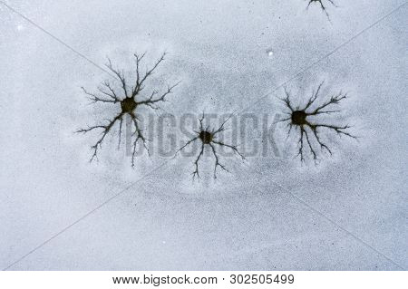 An Aeiral Drone Looking Down Captures Holes And Cracks In Frozen Lake Ice. Dark And Dusty Water Bene