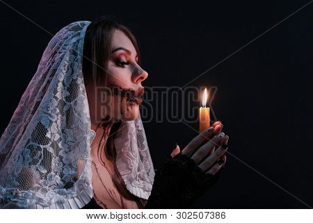 A Beautiful Girl Dressed As A Terrible Nun Holds A Lit Candle. Woman Portrait With Halloween Makeup.