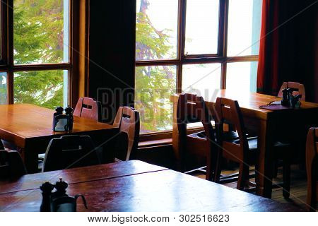 Antique Style Wooden Furniture Including Tables And Chairs Besides A Large Window Taken At A Restaur