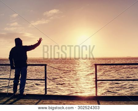 Traveler With Backpack Walk Dificult With Medicine Poles.  Young Tourist On Bridge  Near Sea At The 