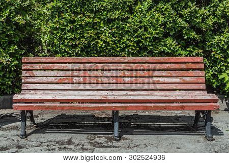 An Old Wooden Painted Brown Color Beautiful Bench With Black Wrought-iron Legs Is By The Walkway In 
