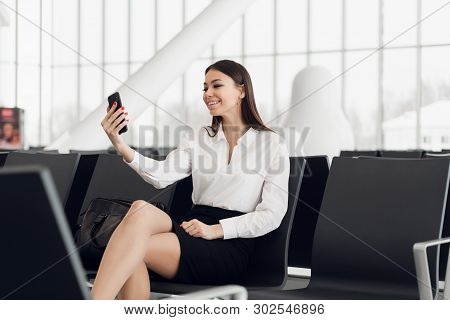 Young Business Woman At International Airport, Making Selfie With Mobile Phone And Waiting For Her F