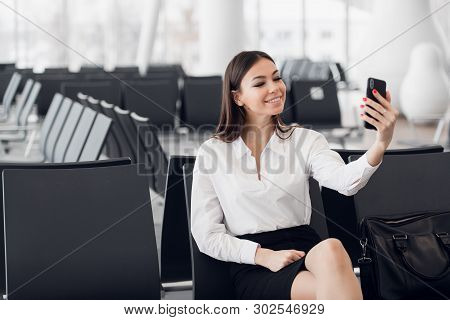 Young Business Woman At International Airport, Making Selfie With Mobile Phone And Waiting For Her F
