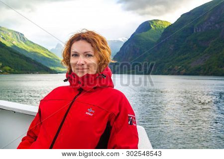 Young Beautiful Woman In Smiling Against The Background Of A Norwegian Fjord. Journey Through Norweg