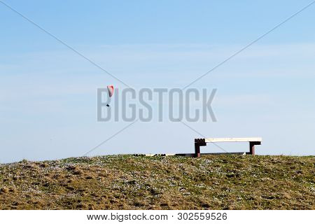 Paraglider On Blue Sky With Empty Bench On Foreground
