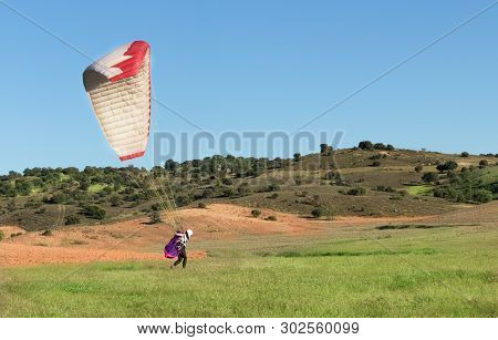Female Pilot Landing With A Paraglider In The Field With A Blue Sky Background
