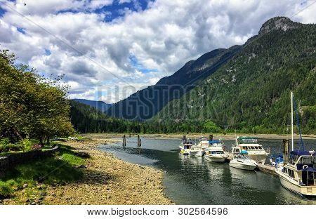 A Faraway View From The Shore Of A Beautiful Marina Full Of Boats And Old Inn, Surrounded By Forest 