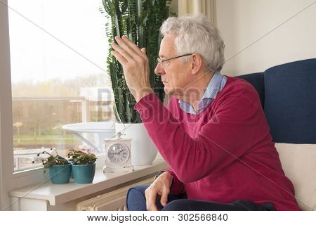 Senior man alone sitting in chair and waving goodbye to somebody outside