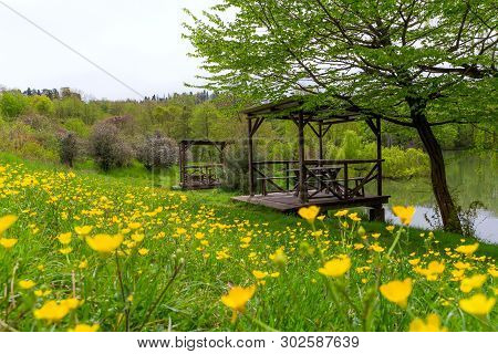 Landscape With Wooden Gazebos By The Lake And Yellow Wildflowers On A Summer Day