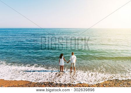 Happy Couple On The Beach With Their Backs To The Camera. Honeymoon Trip. The Couple Are Traveling. 