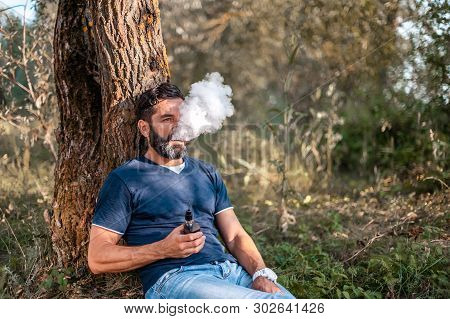 Brutal Smoker Hold And Smoking His E-cigarette Blowing A Stream Of Smoke Spread. Electronic Cigarett