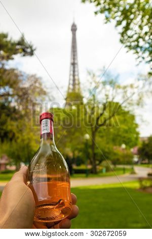 Paris, France - April 9, 2019: Eifel Tower Seen From A Different Angle. Hand Holding A Bottle Of Win