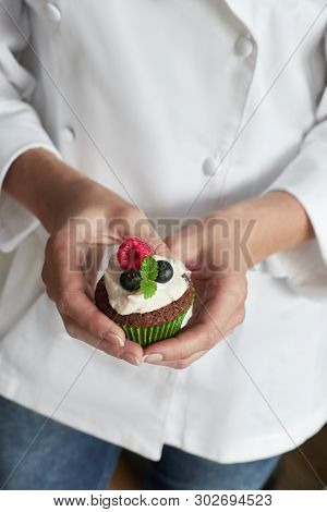 Close-up On Hands Of Female Pastry Chef In White Gown With Muffin Or A Cupcake Decorated With Wild B