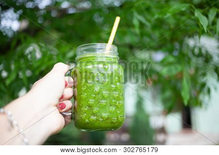woman's hand holding a jar with green cold-pressed juice, nature background. Healthy eating, detoxing, juicing, body cleancing concept 