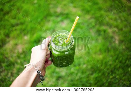 woman's hand holding a jar with green cold-pressed juice, nature background. Healthy eating, detoxing, juicing, body cleancing concept 