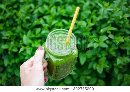woman's hand holding a jar with green cold-pressed juice, nature background. Healthy eating, detoxing, juicing, body cleancing concept 