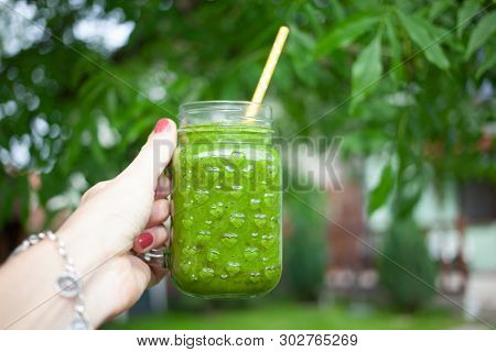 woman's hand holding a jar with green cold-pressed juice, nature background. Healthy eating, detoxing, juicing, body cleancing concept 