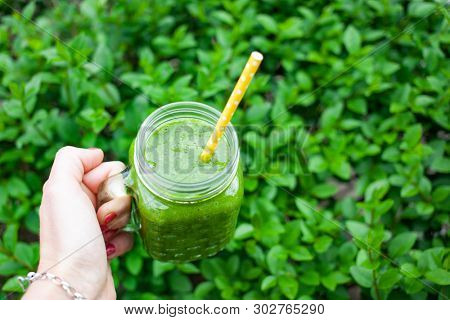 woman's hand holding a jar with green cold-pressed juice, nature background. Healthy eating, detoxing, juicing, body cleancing concept 
