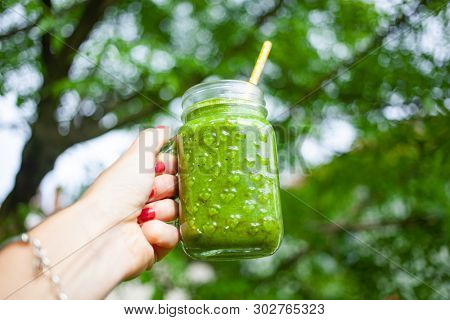 woman's hand holding a jar with green cold-pressed juice, nature background. Healthy eating, detoxing, juicing, body cleancing concept 