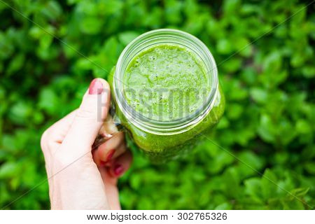 woman's hand holding a jar with green cold-pressed juice, nature background. Healthy eating, detoxing, juicing, body cleancing concept 
