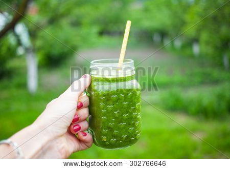 woman's hand holding a jar with green cold-pressed juice, nature background. Healthy eating, detoxing, juicing, body cleancing concept 