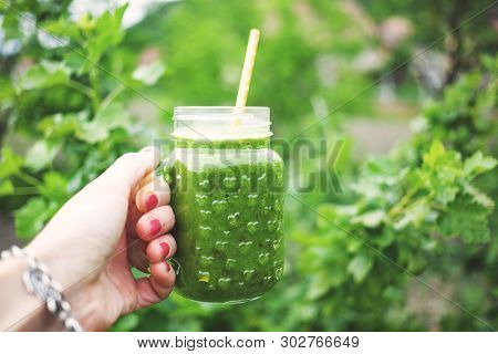woman's hand holding a jar with green cold-pressed juice, nature background. Healthy eating, detoxing, juicing, body cleancing concept 
