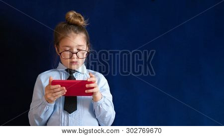 Smart Preschool Girl Holding Smartphone. Expressionless Little Schoolgirl In Eyeglasses Staring In C