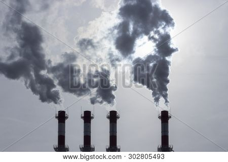 Silhouettes Of Pipes Emitting Dark Steam Into The Atmosphere. Steam Smoke Smog Swirling From Industr