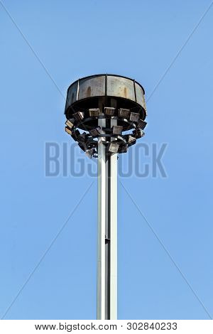 Tower With Reflectors At The Roundabout On The City Road And Street. Lighting Pole With Blue Sky. Bi
