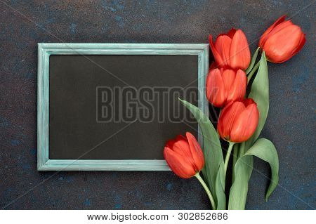 Blackboard And Bunch Of Red Tulips On Abstract Dark Background, Space For Your Test. Flat Lay, Toned