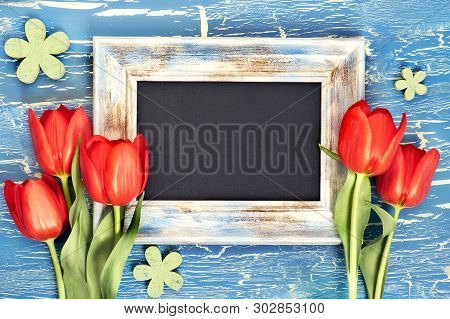 Blackboard And Bunch Of Red Tulips And Lily Of The Valley Flowers On Blue Rustic Background. Space F