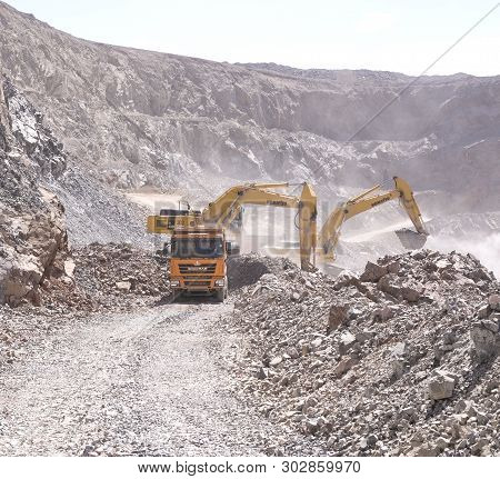 Almaty, Kazakhstan - May 20, 2019: Excavator Loads Soil Into The Yellow Chinese Shacman Dump Truck A