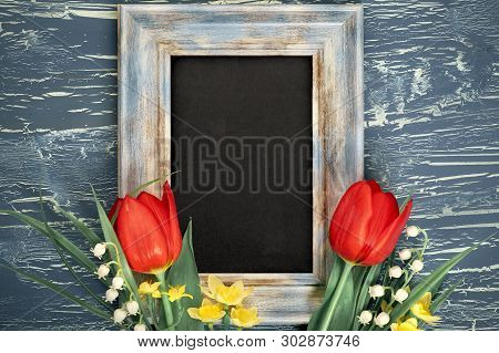 Blackboard And Bunch Of Red Tulips And Lily Of The Valley Flowers On Rustic Background. Space For Yo