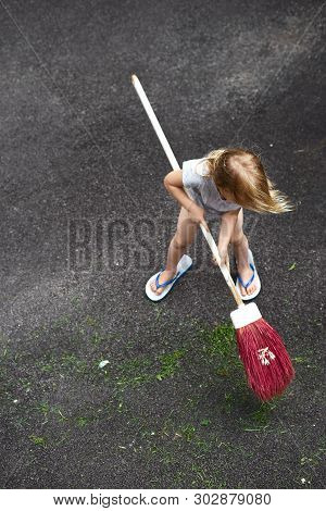 Little Girl Helps Her Parents Collect Grass In The Yard. Seasonal Gardening. Cleaning The Yard