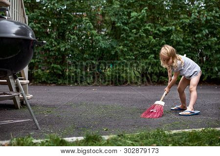 Little Girl Helps Her Parents Collect Grass In The Yard. Seasonal Gardening. Cleaning The Yard