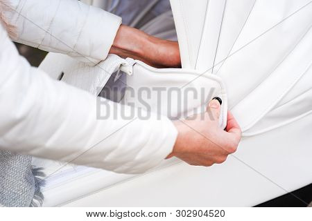 Woman Strolling With White Baby-carriage. Close Up Of Female Hands In White Jacket Fasten Rivet To R