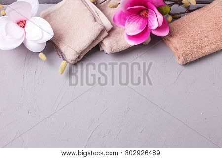 Towels  And Pink Magnolia Flowers On Grey Textured Background. Spa Concept. Selective Focus. Place F