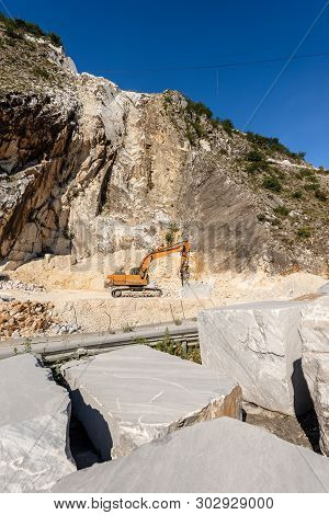 Orange Tracked Excavator With The Jackhammer In A Quarry, Carrara White Marble In The Apuan Alps (al