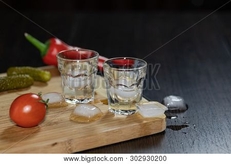 Two Shot Glasses Of Vodka On The Cutting Board With Cherry Tomatoes, Marinated Cucumbers, Pepper And