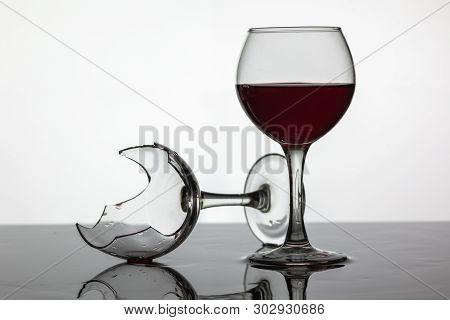 Filled With A Glass Of Wine And Broken Wine Glass With Red Wine Which Is Laying On The Wet Surface. 