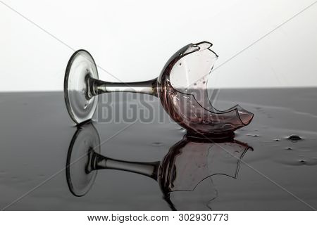 Broken Wine Glass With Red Wine Which Is Laying On The Wet Surface. White Background