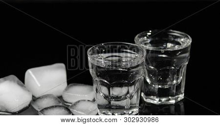 Vodka In Shot Glasses With Ice Cubes Placed On A Black Background.