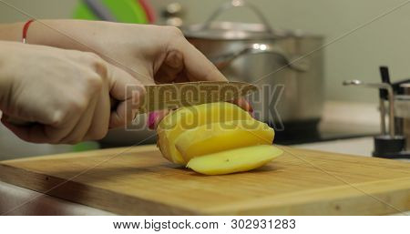 Female Housewife Hands Slicing Potatoes Into Pieces On The Wooden Cutting Board In The Kitchen