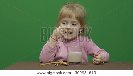 The Child Eats Cookies. A Little Girl Is Eating Cookies And Drink Cacao Sitting On The Table. Green 